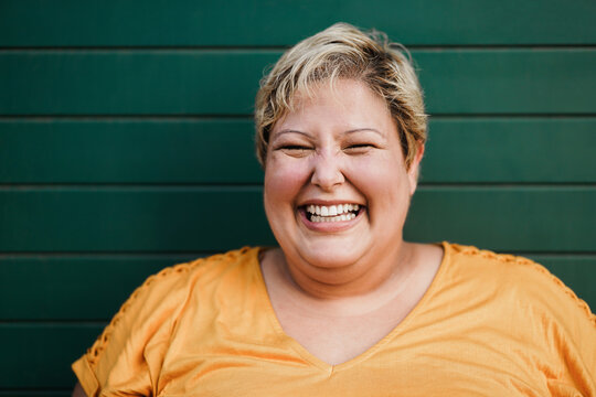 Portrait of curvy woman smiling on camera outdoors with green background - Focus on face