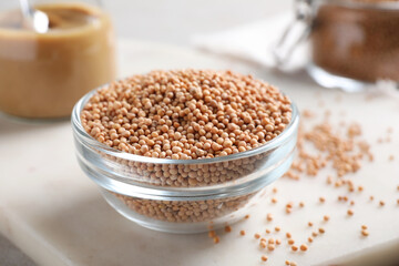 Mustard seeds in glass bowl on board, closeup.