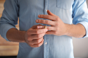 Man taking off wedding ring on blurred background, closeup. Divorce concept - obrazy, fototapety, plakaty