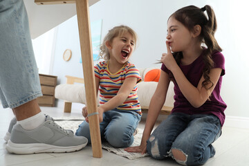 Cute little children tying shoe laces of their father together at home, closeup