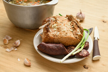 baked meat and blood sausage on a plate, green onion and garlic on wooden background, home cooking