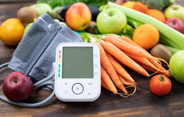 Blood pressure monitor and fresh fruits with vegetables against wooden table. Healthy lifestyle and...