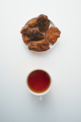 Chaga, birch tree mushroom in white plate and chaga tea on blue background. Natural medicine, antioxidant, superfood. Vertical.