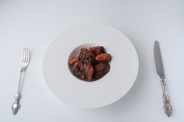 Chaga, birch tree mushroom in white plate with silver knife and fork on blue background. Natural medicine, antioxidant, superfood.