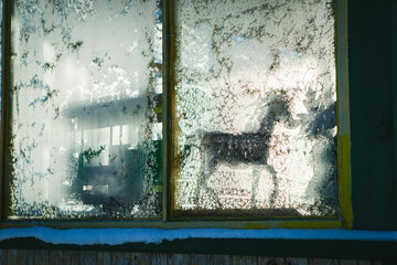 Silhouette of horse toy on sill behind window. Frost patterns on glass
