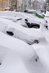 Parked cars covered with snow on an uncleaned snowy road after snowfall. Bad winter weather, increased precipitation and snow levels concept. 