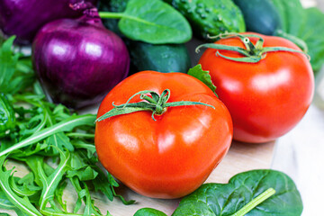 Fresh farm summer vegetables for salad: cucumbers, tomatoes, onions, arugula leaves in the kitchen on light background.