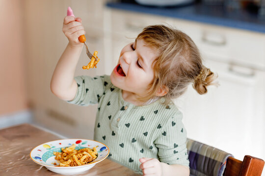 Adorable toddler girl eat pasta macaroni bolognese with minced meat. Happy child eating fresh cooked healthy meal with noodles and vegetables at home, indoors.