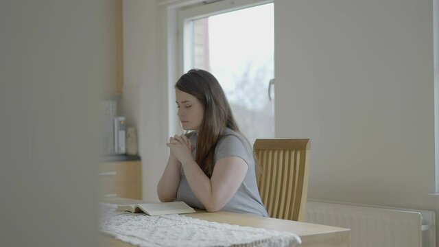 Woman praying or meditating sit by a wooden table in her kitchen