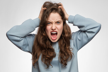 The young woman is angry and screaming, holding her head. Young girl with long hair and blue...