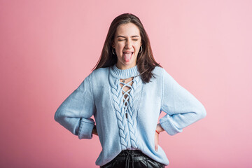 Happy brunette teen girl showing tongue in studio on pink background