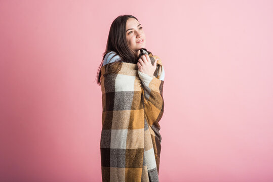 Portrait of a brunette girl who is wrapped in a blanket in the studio on a pink background
