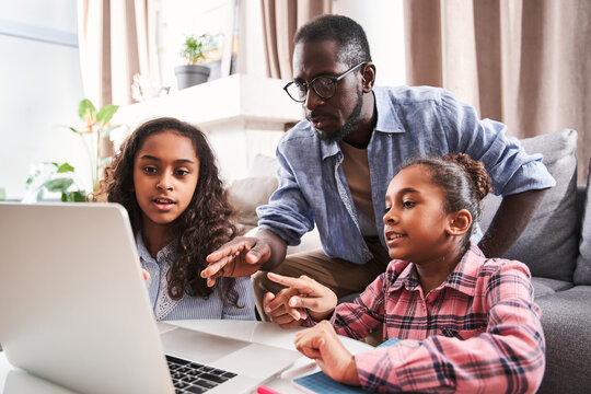 Girls doing homework with their positive bearded father