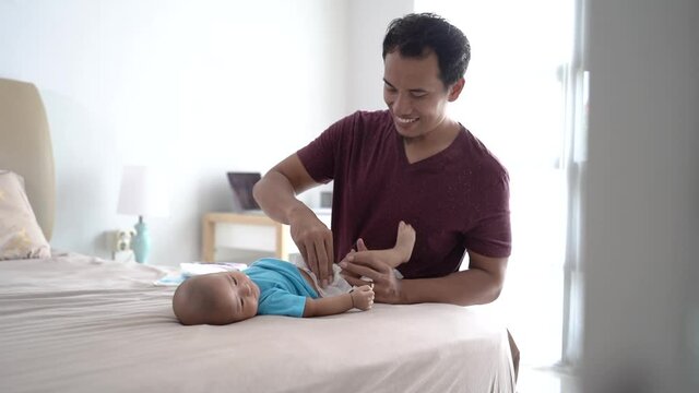 portrait of asian father changing his infant baby diaper at home