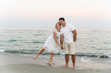 a guy with a girl in summer clothes are walking by the ocean. husband and wife at a romantic sunset of the day near the sea. lovers run along the beach. honeymoon for the newlyweds.
