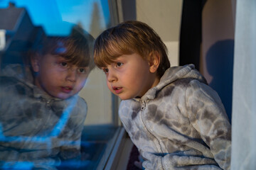 Little toddler boy is lying on a carpet in a room near window. Child wearing warm soft jumpsuit looking at the window with interest. © Anna