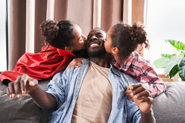 Obraz premium Father sitting at the sofa while his daughters kissing him