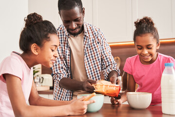 Father lovingly imposes granola or flakes at the plates to his daughters