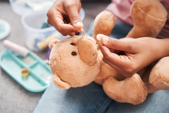 Girl feeling involved in repairing her toy and sewing while sitting at home
