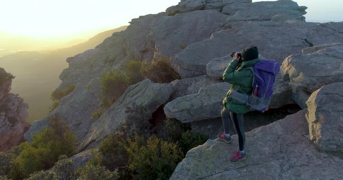 mujer escaladora con mochila haciendo fotografías al amanecer en la cima de una montaña