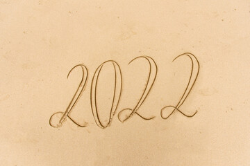 2022 year message handwritten on the sand beach background. New Year concept.