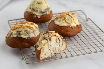 Close-up of delicious cinnabons on a cooling tray on white marble background. One is cut in half. Cinnamon rolled buns with white sticky glaze, almond flakes and caramel on top. Dessert buns pastry.