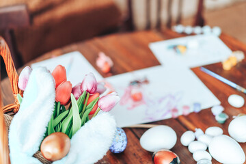 Preparing decorations for Easter. On the table are paints with brushes, a basket with Easter eggs and bunny ears