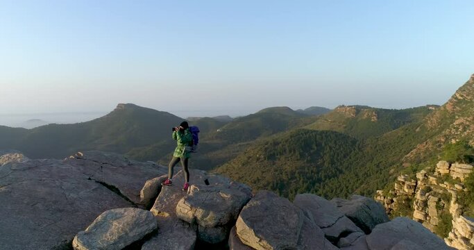 Joven mujer fotografiando desde la cima de una monta&ntilde;a al amanecer