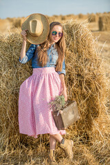 girl in a wheat field wearing hat and sunglasses and holding suitcase