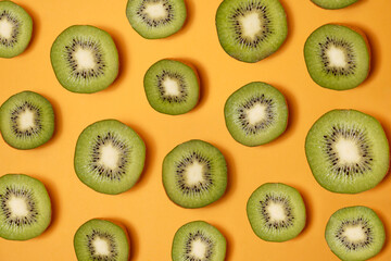 Fototapeta premium Kiwi fruit slice isolated on yellow background. Fresh kiwi fruit slice pattern on yellow background. Multicolored kiwifruit of different sizes neatly arranged on a yellow background. From the top view