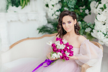 An attractive young woman holds a bouquet of white and purple tulips in her hands. Beautiful girl in a lush dress