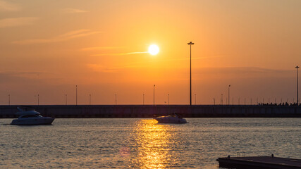 Two boats sail towards each other along the pier across the sea illuminated by the glare of the setting sun