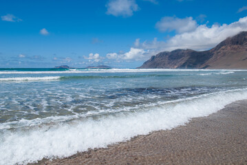 glasklares Wasser spült in Wellen an den Sandstrand Playa de Famara mit Blick auf die Insel La Graciosa, Lanzarote, Kanaren
