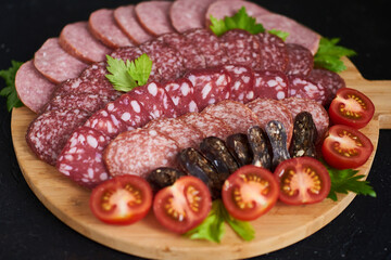 Assorted sliced sausages of different flavors. Served on a beautiful wooden tray, with herbs and cherry tomatoes