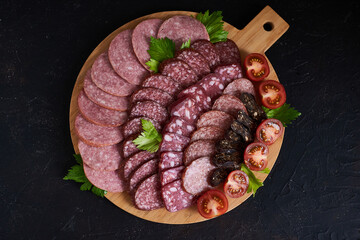 Assorted sliced sausages of different flavors. Served on a beautiful wooden tray, with herbs and cherry tomatoes