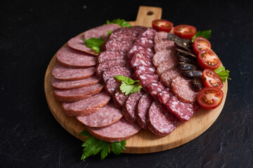 Assorted sliced sausages of different flavors. Served on a beautiful wooden tray, with herbs and cherry tomatoes