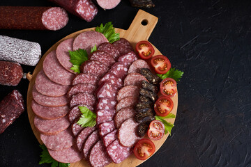 Assorted sliced sausages of different flavors. Served on a beautiful wooden tray, with herbs and cherry tomatoes