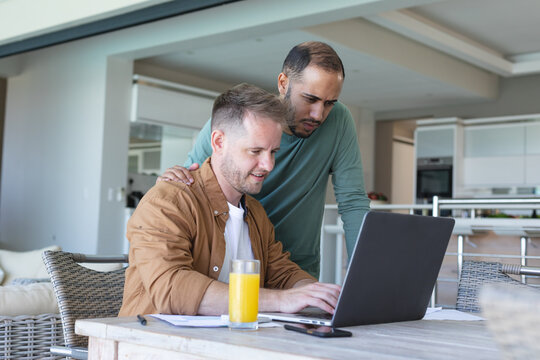 Multi Ethnic Gay Male Couple Going Through Bills And Using Laptop At Home