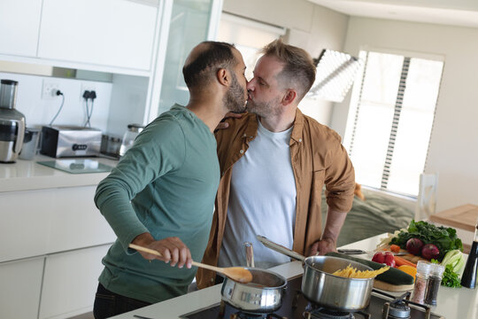 Multi ethnic gay male couple preparing food together and kissing at home