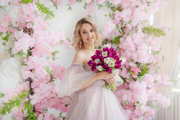 Obraz na płótnie Canvas Beautiful girl in a lush pink dress in a photo studio. Bouquet of tulips. Blonde girl with tulips. An attractive young woman holds a bouquet of white and purple tulips in her hands.