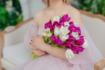 Beautiful girl in a lush pink dress in a photo studio. Bouquet of tulips. Blonde girl with tulips. An attractive young woman holds a bouquet of white and purple tulips in her hands.