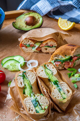 Stuffed toasted bagel sandwich cut into half with avocado, mayo, cucumber, lettuce and onions....