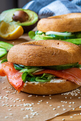 Homemade bagel sandwiches. Gluten free toasted bagel with smoked salmon, cream cheese, cucumber and lettuce. Avocado bagel in the background on a baking sheet. Healthy breakfast, fun vibrant colors