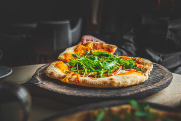 woman Hand takes a slice of Pepperoni Pizza with Mozzarella cheese, salami, Tomatoes, pepper, Spices and Fresh arugula in cafe