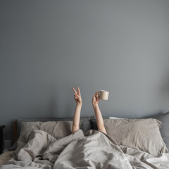 Woman laying in bed, holding mug with coffee in hand and show 