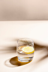 Glass of water with lemon  on beige background with hard light and shadow