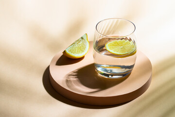 Glass of water with lemon  on beige background with hard light and shadow