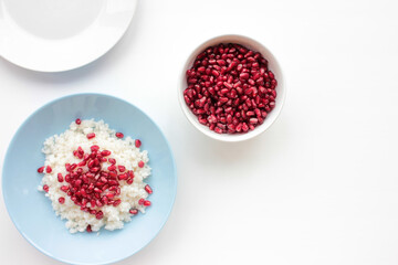 Middle eastern rice pilaf with raw pomegranate seeds in a blue bowl on white background. Flat lay food composition. Top view, copy space. 
