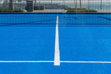 Bright blue tennis, paddle ball or pickleball court ground view with white line towards black net outdoors.