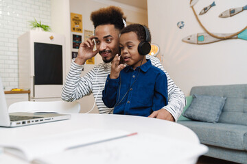 Happy african american father and son in headphones using laptop at home